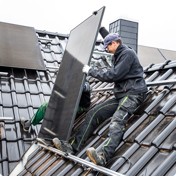 Ein junger Mann montiert ein PV-Modul auf einem Dach