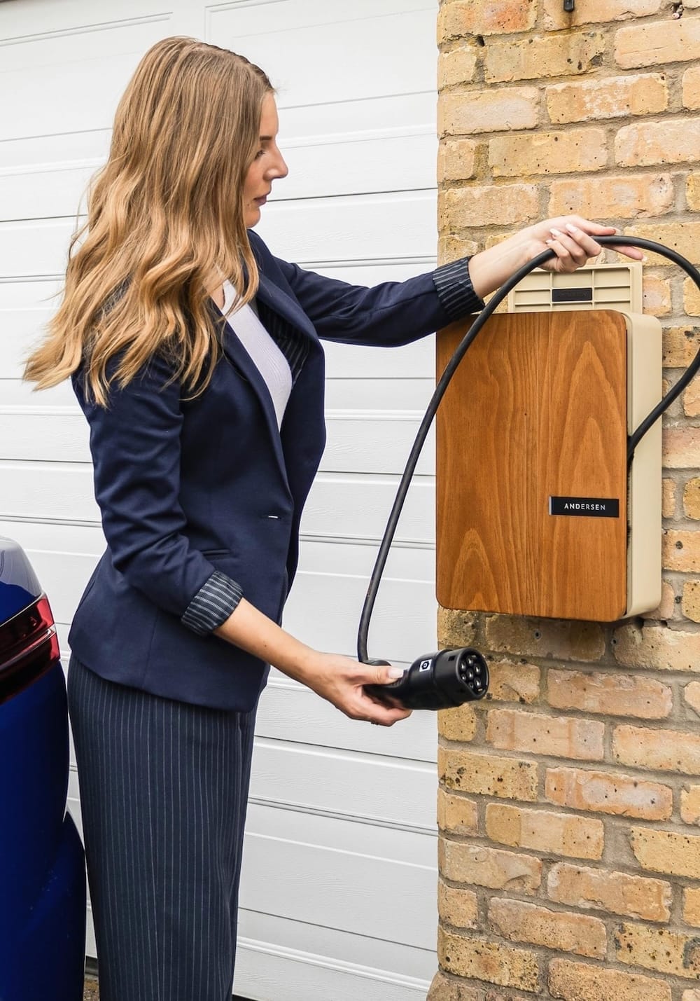 Eine Frau in Business-Kleidung rollt ein Kabel aus einer Wallbox um ihr E-Auto zu laden Eine Frau in Business-Kleidung rollt ein Kabel aus einer Wallbox um ihr E-Auto zu laden