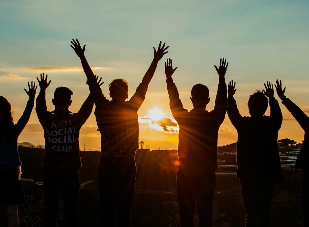 Ein Team steht mit dem Rücken zur Kamera auf einer Wiese und beobachtet freudig den Sonnenaufgang Ein Team steht mit dem Rücken zur Kamera auf einer Wiese und beobachtet freudig den Sonnenaufgang