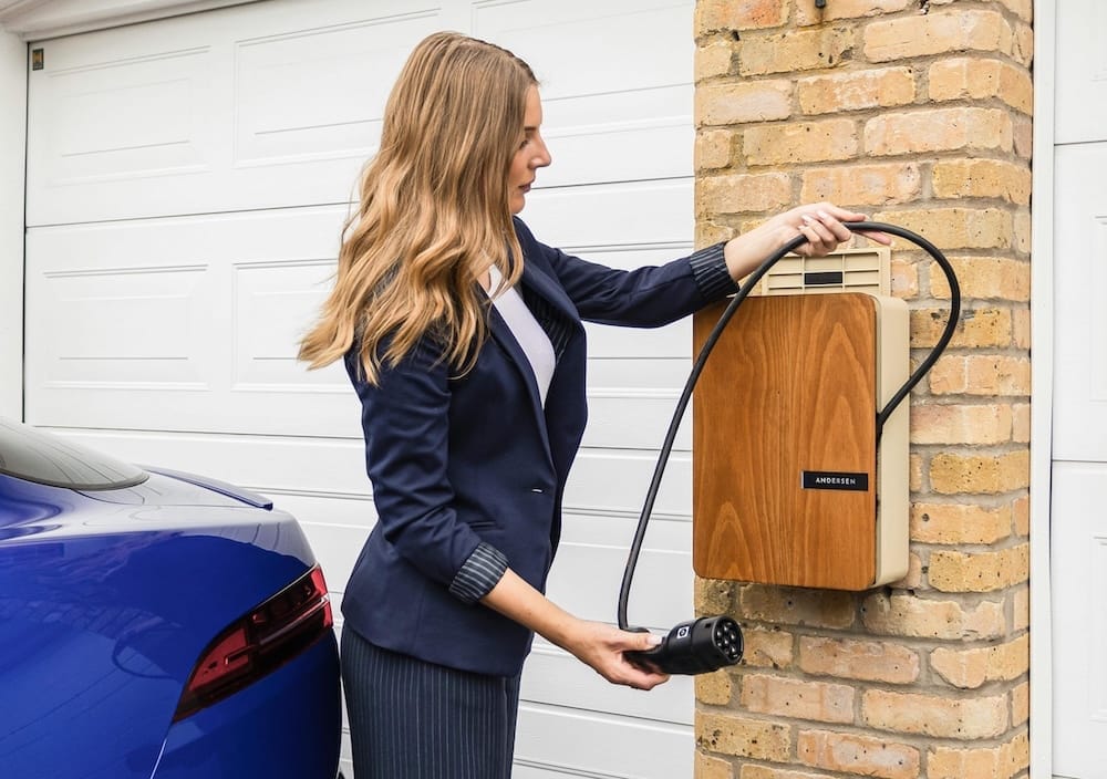 Eine Frau in Business-Kleidung rollt ein Kabel aus einer Wallbox um ihr E-Auto zu laden Eine Frau in Business-Kleidung rollt ein Kabel aus einer Wallbox um ihr E-Auto zu laden